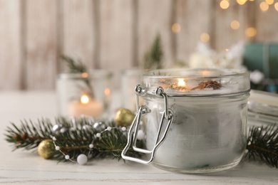 Burning scented conifer candle and Christmas decor on white wooden table. Space for text