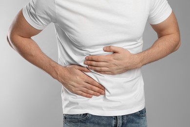 Man suffering from pain in lower right abdomen on light grey background, closeup. Acute appendicitis