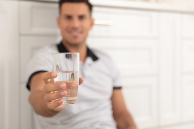 Man holding glass of pure water in kitchen, focus on hand. Space for text