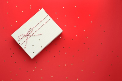 Gift box and confetti stars on red background, flat lay. Christmas celebration