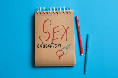 Notebook with phrase "SEX EDUCATION" and gender symbols on blue background, flat lay