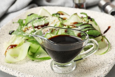 Gravy boat of balsamic vinegar on plate with vegetable salad, closeup