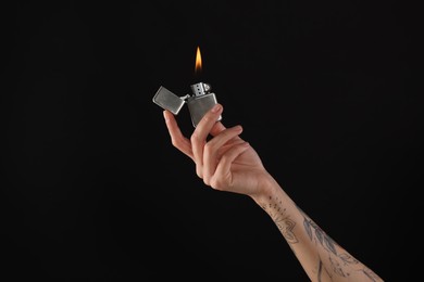 Woman holding lighter with burning flame on black background, closeup