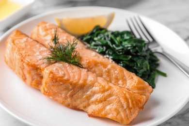 Tasty salmon with spinach and lemon on plate, closeup