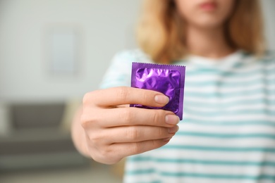 Woman holding condom indoors, closeup. Safe sex concept