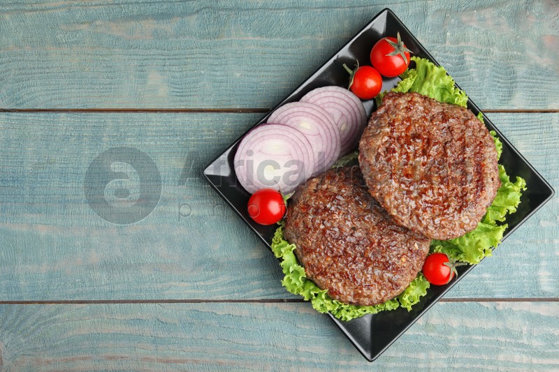Grilled meat cutlets for burger on blue wooden table, top view. Space for text