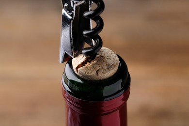 Opening wine bottle with corkscrew on blurred background, closeup