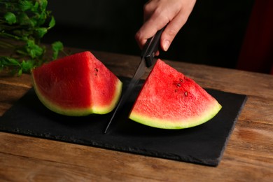 Woman cutting delicious watermelon on slate board at wooden table, closeup