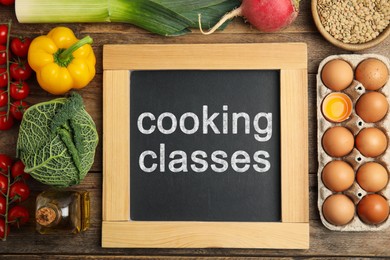 Small chalkboard with inscription Cooking Classes and different fresh products on wooden table, flat lay