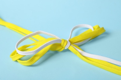 Yellow and white shoe laces tied in bow on light blue background, closeup