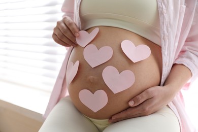 Pregnant woman with heart shaped sticky notes on belly indoors, closeup. Choosing baby name