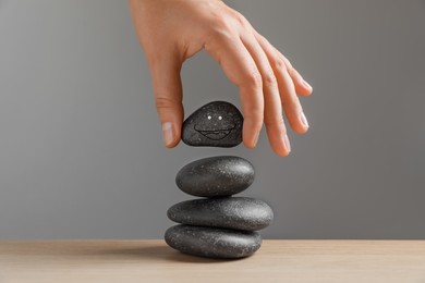 Woman putting stone with drawn happy face on stack against grey background, closeup. Zen concept