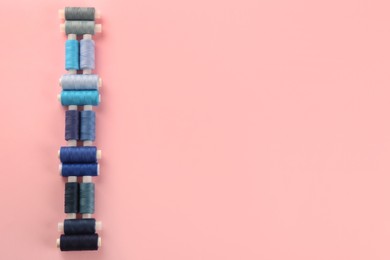 Photo of Different shades of blue sewing threads on pink background, flat lay. Space for text