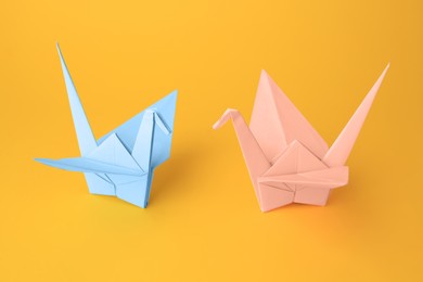 Photo of Origami art. Beautiful light blue and pale pink paper cranes on orange background