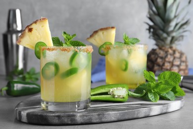 Photo of Glasses of spicy pineapple cocktail with jalapeno and mint on grey table