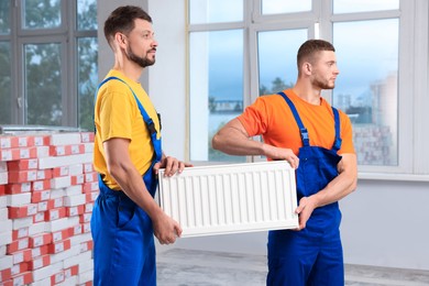 Professional plumbers with new heating radiator indoors