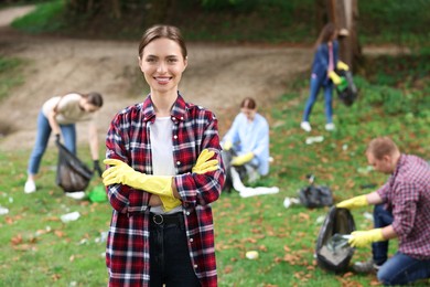 Photo of Young woman in gloves and group of people collecting garbage outdoors