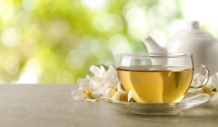 Cup of jasmine tea and fresh flowers on grey table outdoors, space for text. Banner design