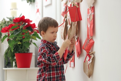 Cute little boy taking gift from Advent calendar at home. Christmas tradition