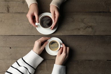 Photo of Women with cups of aromatic coffee at wooden table, top view. Space for text