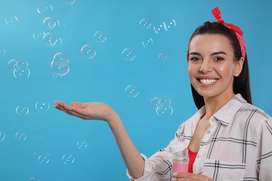 Photo of Young woman having fun with soap bubbles on light blue background, space for text