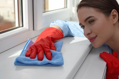Young woman cleaning window sill with rag at home