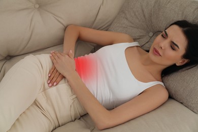 Woman suffering from appendicitis inflammation on sofa indoors