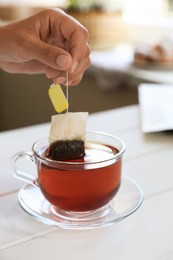 Woman taking tea bag out of cup at white wooden table indoors, closeup