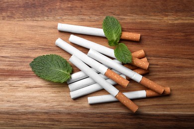 Menthol cigarettes and mint leaves on wooden table, flat lay