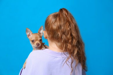 Photo of Little girl with her Chihuahua dog on light blue background, back view. Childhood pet