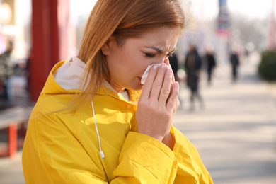 Sick woman sneezing on city street. Influenza virus