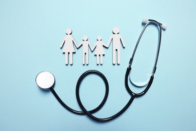 Photo of Figures of family near stethoscope on light blue background, flat lay. Insurance concept