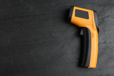 Modern non-contact infrared thermometer on black slate background, top view. Space for text