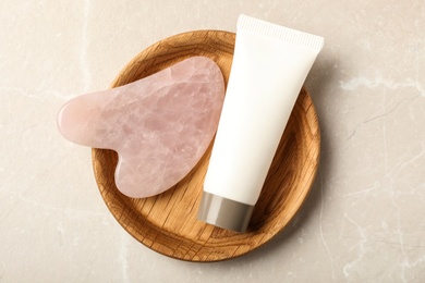 Photo of Rose quartz gua sha tool and cosmetic product on grey table, top view
