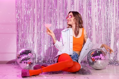 Photo of Beautiful woman in stylish outfit with glass of drink among disco balls at party indoors