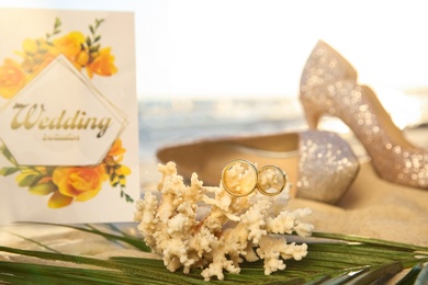 Coral with gold rings and wedding invitation on sandy beach