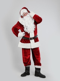 Santa Claus with headphones listening to Christmas music on light grey background