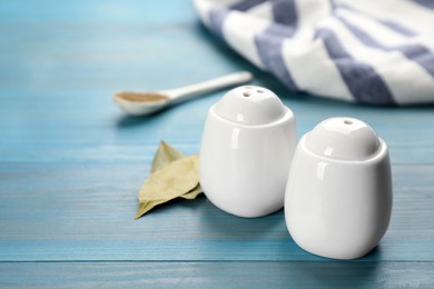 Photo of White ceramic salt and pepper shakers with bay leaves on turquoise wooden table, space for text