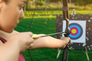Woman with bow and arrow aiming at archery target in park, closeup