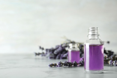 Photo of Bottle of natural essential oil and lavender flowers on grey marble table. Space for text