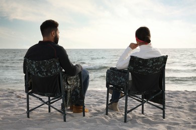 Couple sitting in camping chairs and enjoying seascape on beach, back view