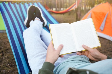 Man with book resting in comfortable hammock outdoors, closeup
