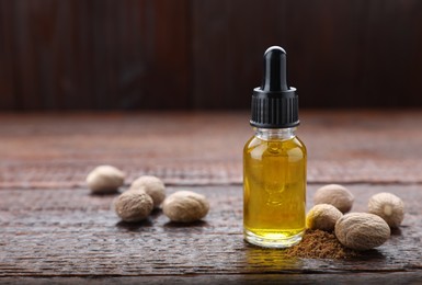 Photo of Bottle of nutmeg oil and nuts on wooden table, space for text