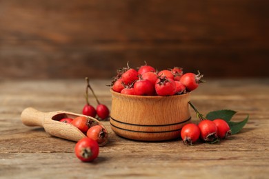 Ripe rose hip berries with green leaves and scoop on wooden table