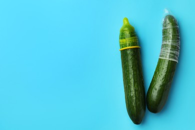 Cucumbers with condoms on light blue background, flat lay and space for text. Safe sex concept