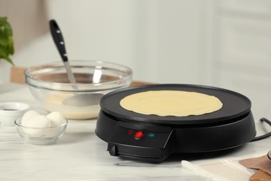 Photo of Electric maker with crepe and ingredients on white marble table in kitchen