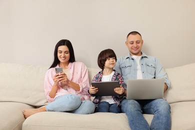 Happy family with gadgets on sofa at home
