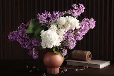 Beautiful lilac flowers in vase, twine and book on wooden table