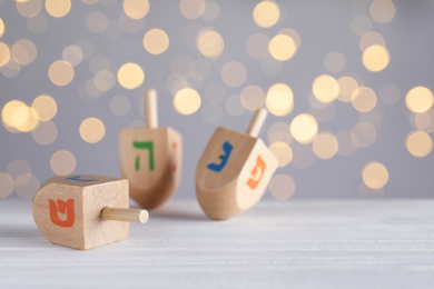 Hanukkah traditional dreidels on white wooden table against blurred lights. Space for text