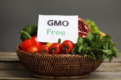 Tasty fresh GMO free products and paper card on wooden table against grey background